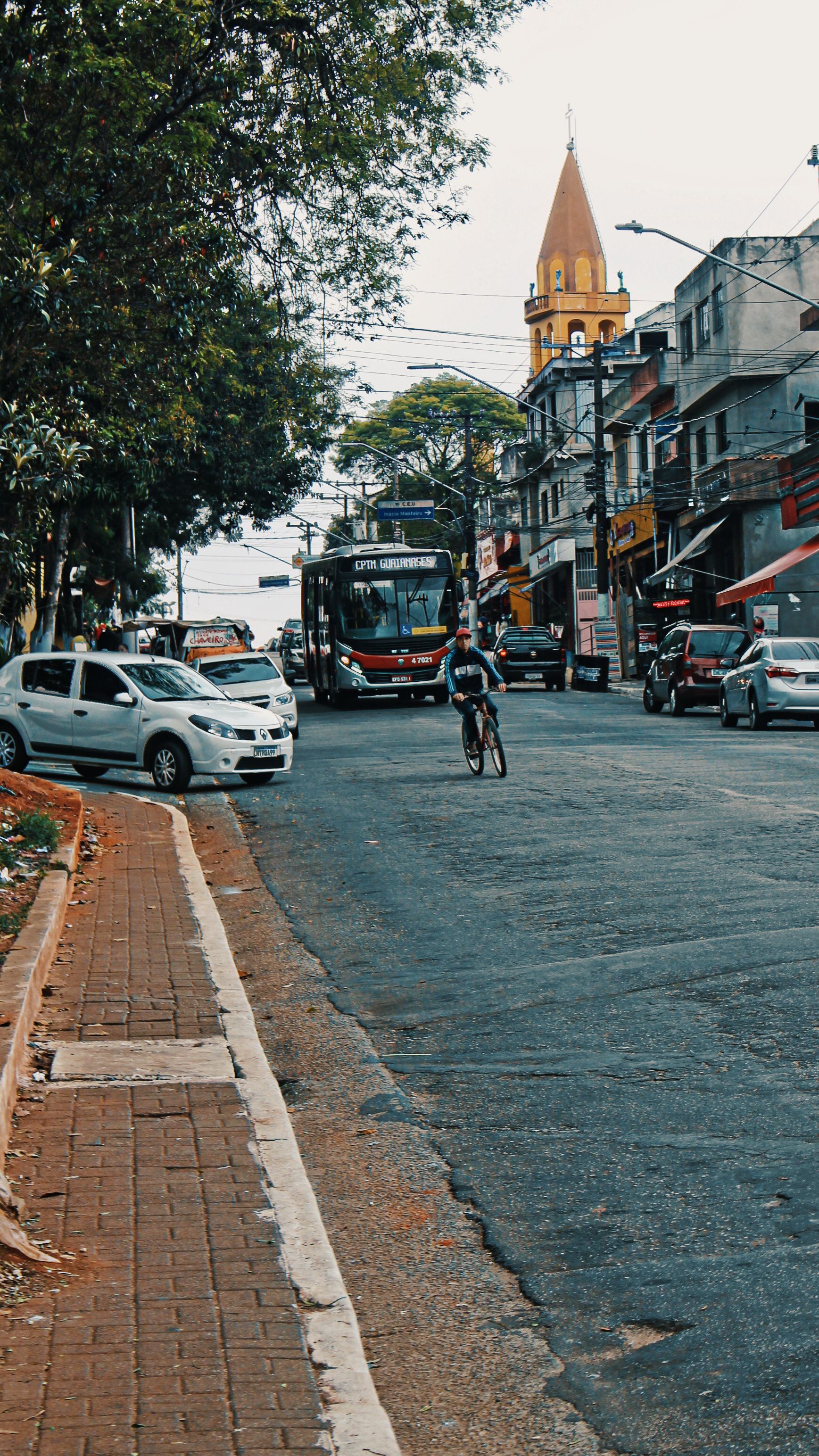 Busy city street featuring a cyclist navigating through traffic with parked and moving vehicles.