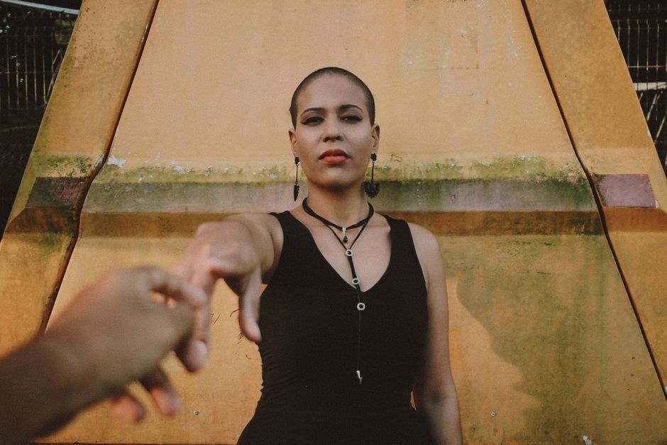 A woman in a black dress reaching out, set against an urban outdoor backdrop.
