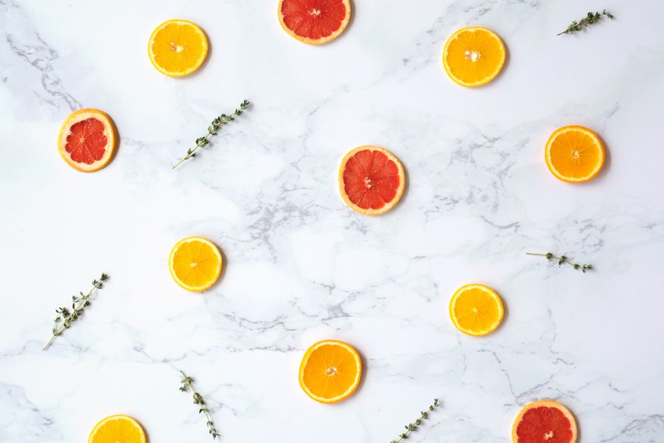 Artistic flatlay of orange and grapefruit slices on a marble background with herbs. Perfect for food styling.