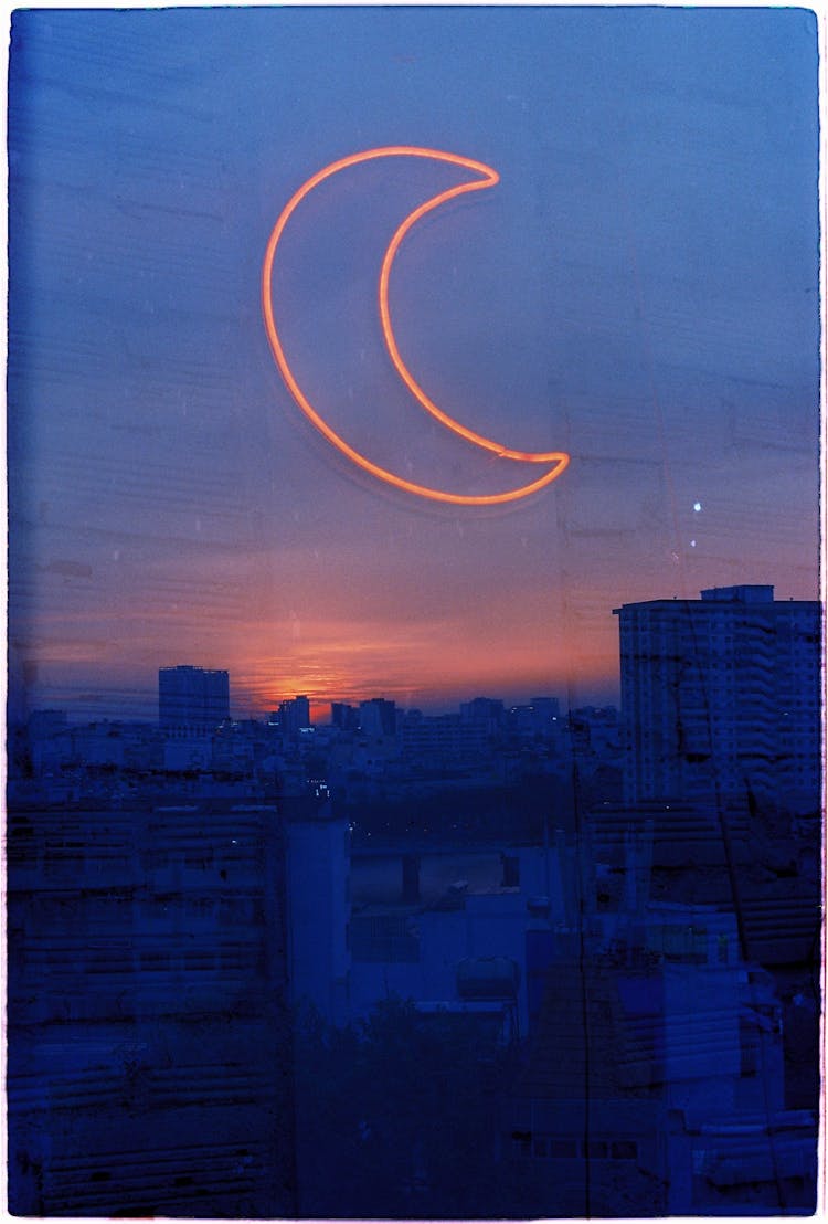 Neon Light In A Moon Shape On A Window And Reflection Of Urban Buildings At Sunset 