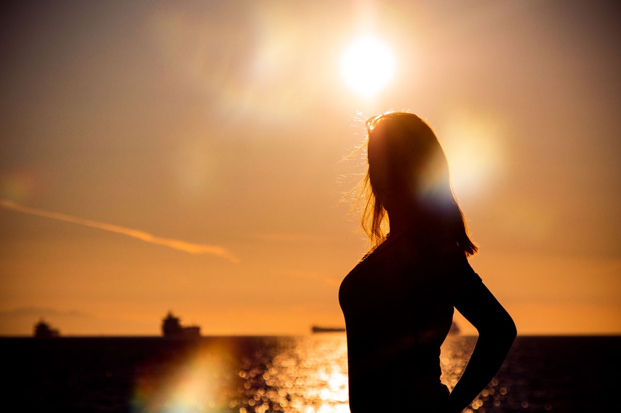 a beautiful silhouette of a woman posing by the sea with a radiant sun