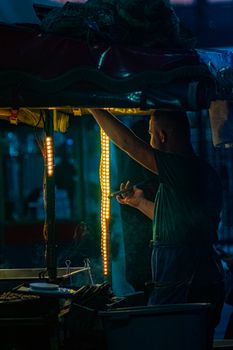 A man cooking at an illuminated street food stall during the night, creating a vibrant street scene.