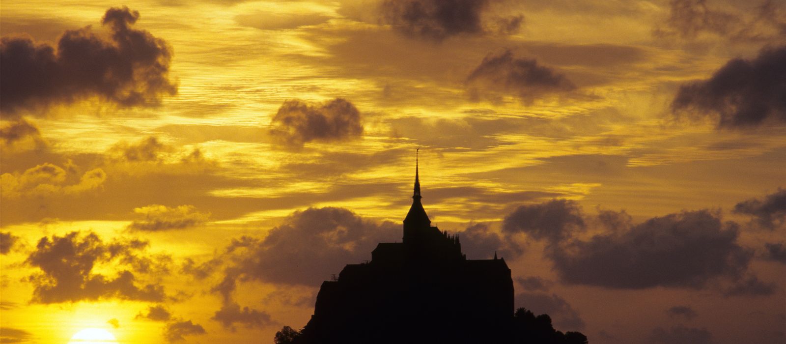 Dramatic silhouette of Mont Saint-Michel during a vibrant sunset in Normandy, France.