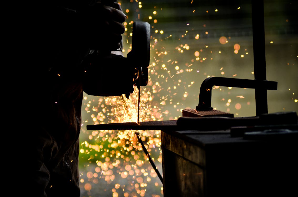 Free A silhouette of a worker using a welding tool emitting bright sparks in a workshop setting. Stock Photo