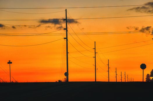 Silhouetted electrical poles against a vibrant sunset sky in Plainview, Minnesota.