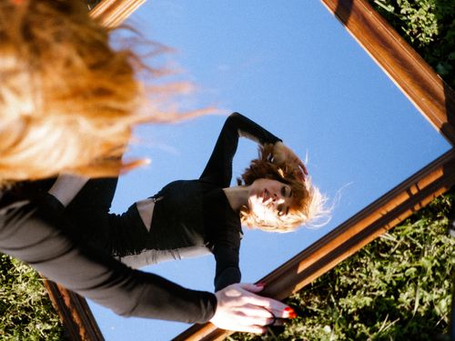 Free Artistic portrait of a woman reflected in a mirror against the sky, creating an engaging visual twist. Stock Photo