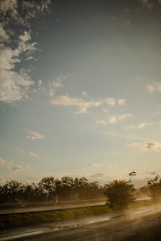 A scenic view of a wet road under a partly cloudy blue sky and green trees.