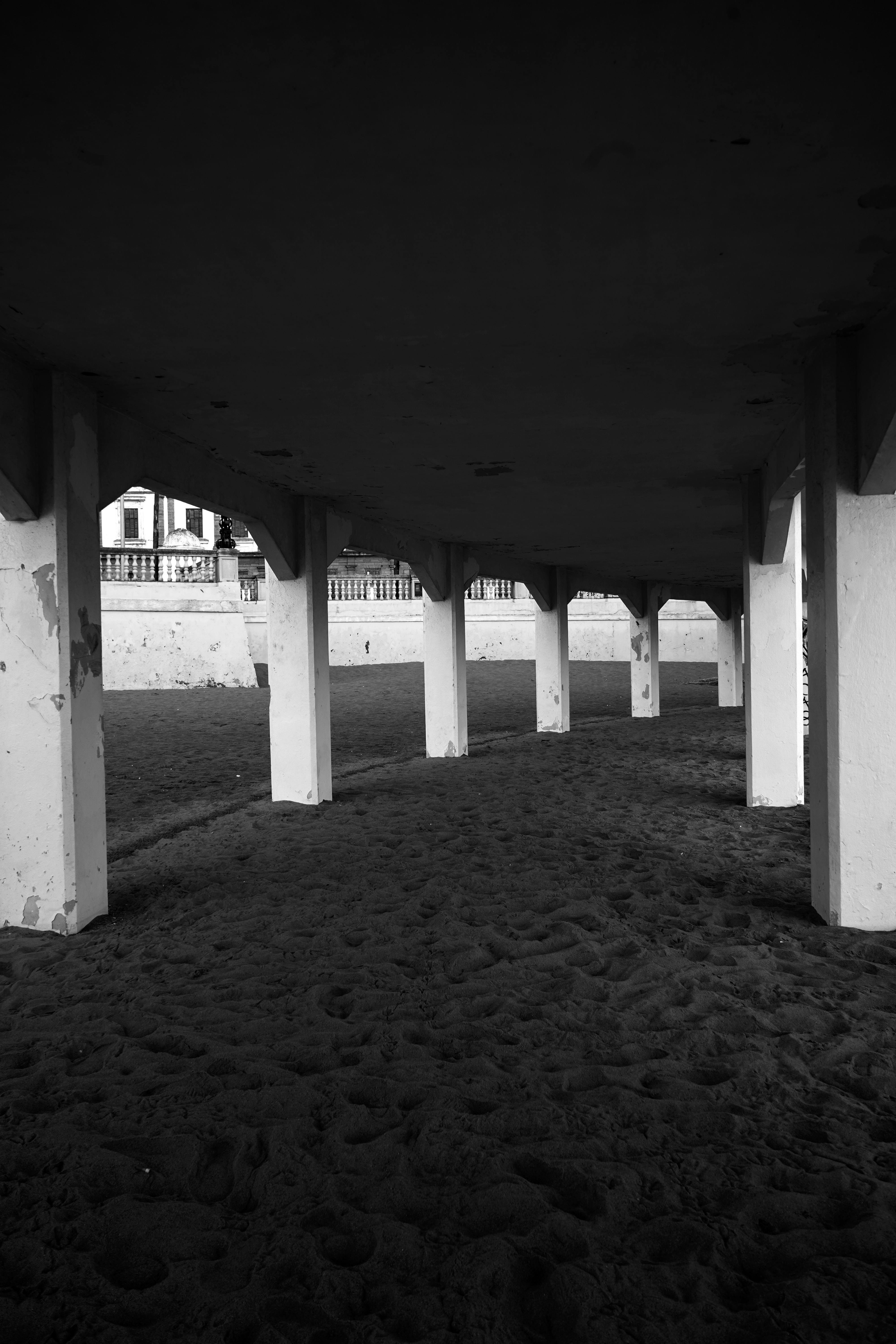 Black and white photo of a colonnade on a sandy beach, offering a dramatic architectural view.
