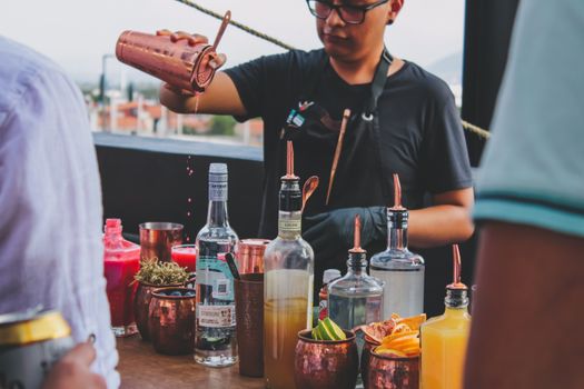 A bartender expertly pours drinks at an outdoor bar with colorful cocktail ingredients.
