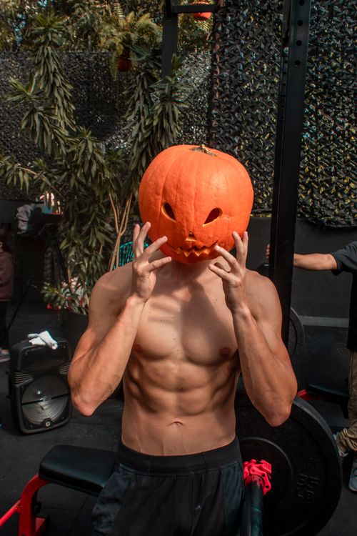 Free Topless male with a pumpkin head posing in a gym setting, celebrating Halloween. Stock Photo