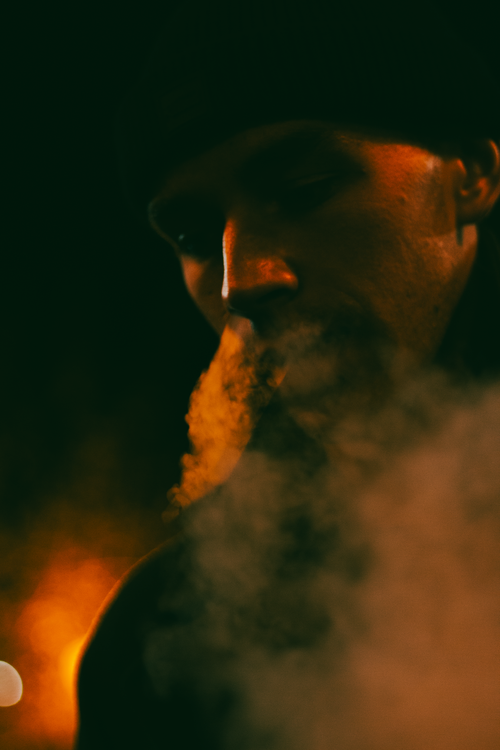 Free A dramatic close-up of a man exhaling smoke in low light, creating a moody and mysterious atmosphere. Stock Photo