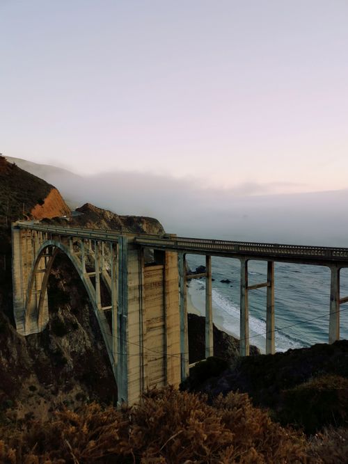 Free A stunning view of Bixby Creek Bridge over rugged cliffs and ocean at sunset in Big Sur, California. Stock Photo