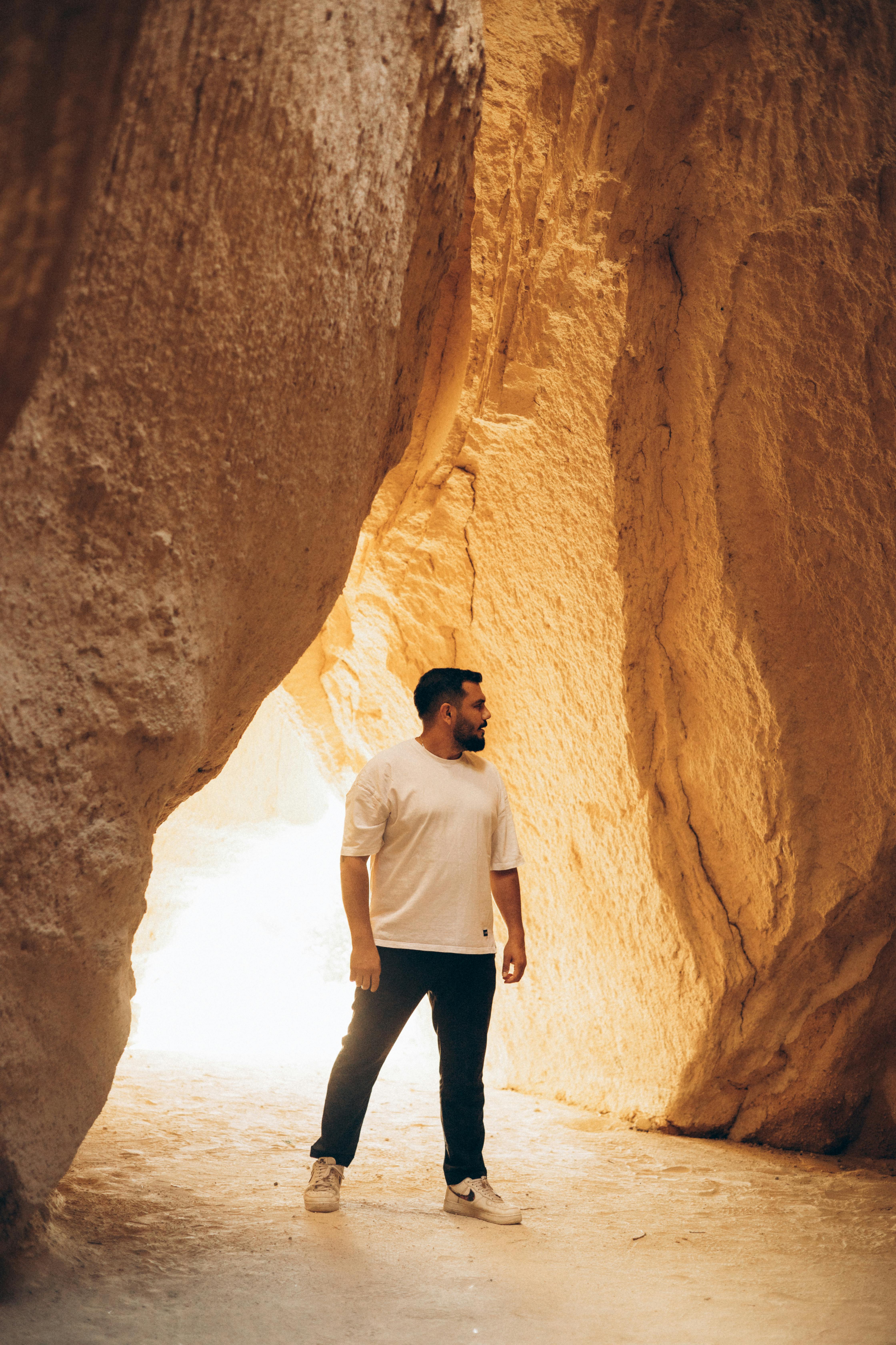 A man in a white t-shirt explores a sunlit rocky cave, highlighting adventure and discovery.