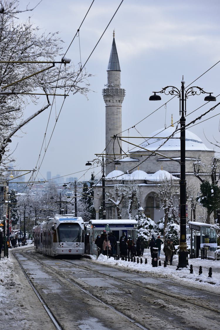 Tram Standing On Tram Stop By Building With Tall Tower