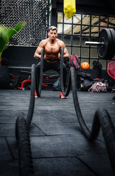 Tattooed man performs exercise with battle ropes in Ciudad de México gym, showcasing strength and fitness.