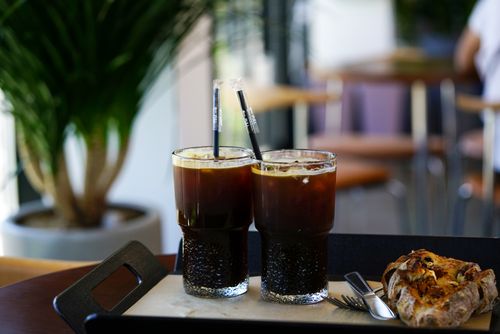 Free Two glasses of iced coffee with straws and pastry on a tray in a cozy cafe setting. Stock Photo