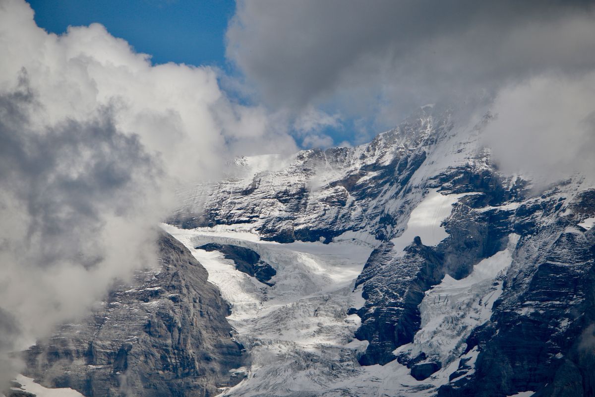 Snow and glacier ice on dark rock peaks, with cloud rolling across them