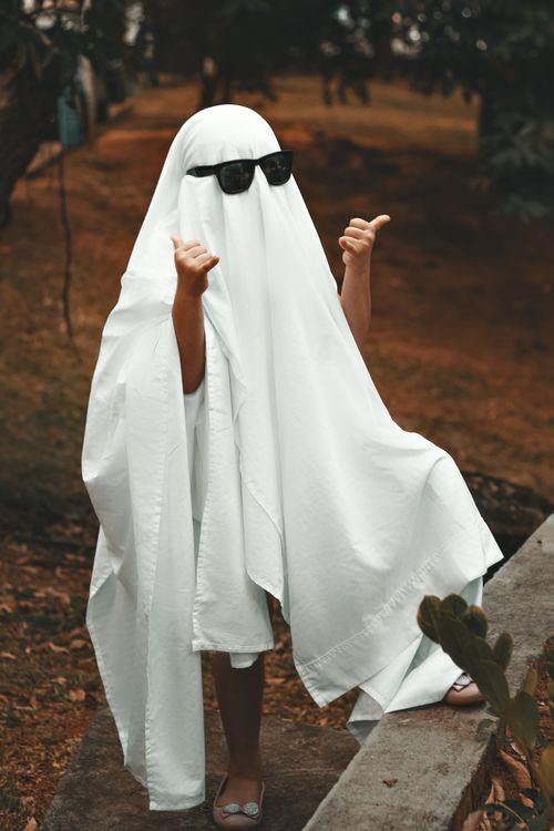 Free Child dressed as a ghost with sunglasses, making a fun gesture outdoors. Stock Photo