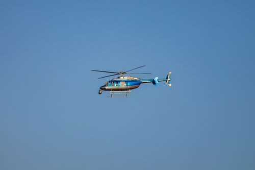 Free A blue helicopter in flight against a clear blue sky, showcasing smooth aerial maneuvering. Stock Photo