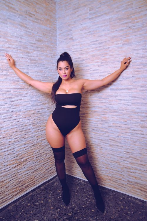 Free Confident woman posing indoors in a stylish black outfit against a textured wall. Stock Photo