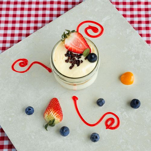 Free Flat lay of a creamy fruit dessert in a mason jar with strawberries and blueberries on a tabletop. Stock Photo