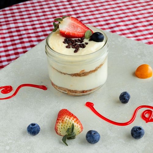 Free A creamy dessert jar topped with fresh strawberries and blueberries on a stylish checkered table. Stock Photo