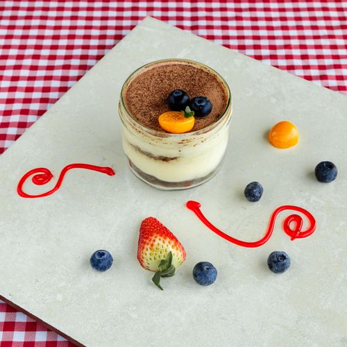 Free Homemade tiramisu in glass jar with fresh blueberries and strawberries on checkered tablecloth. Stock Photo