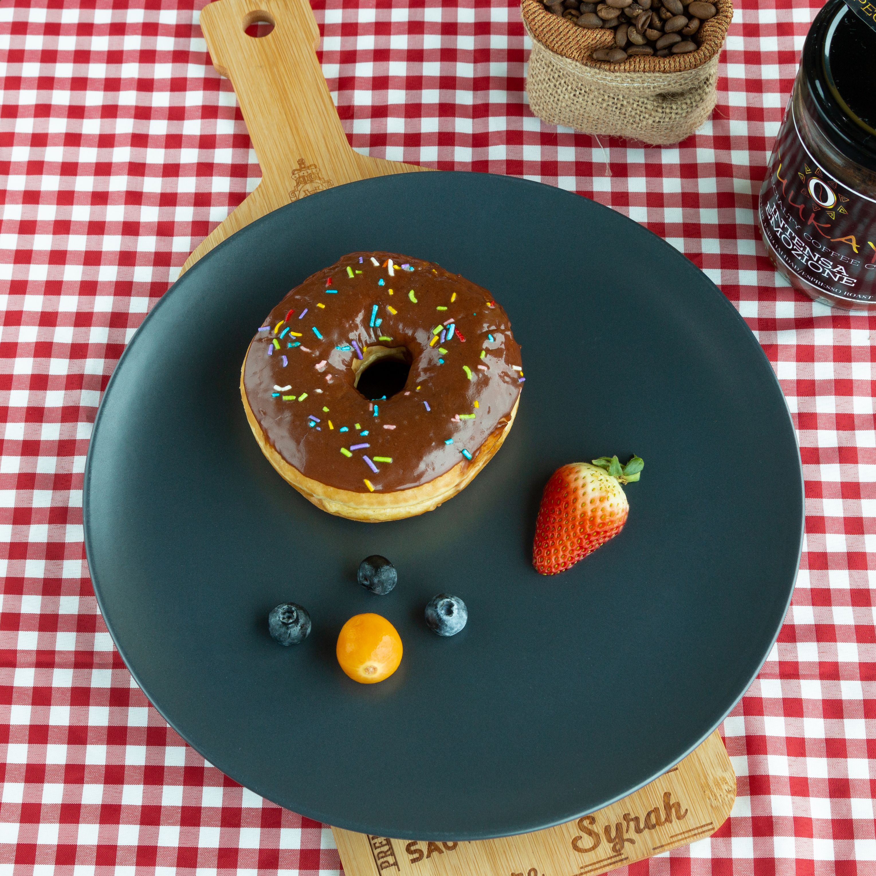 A scrumptious chocolate donut with a side of fresh berries on a stylish plaid tablecloth.