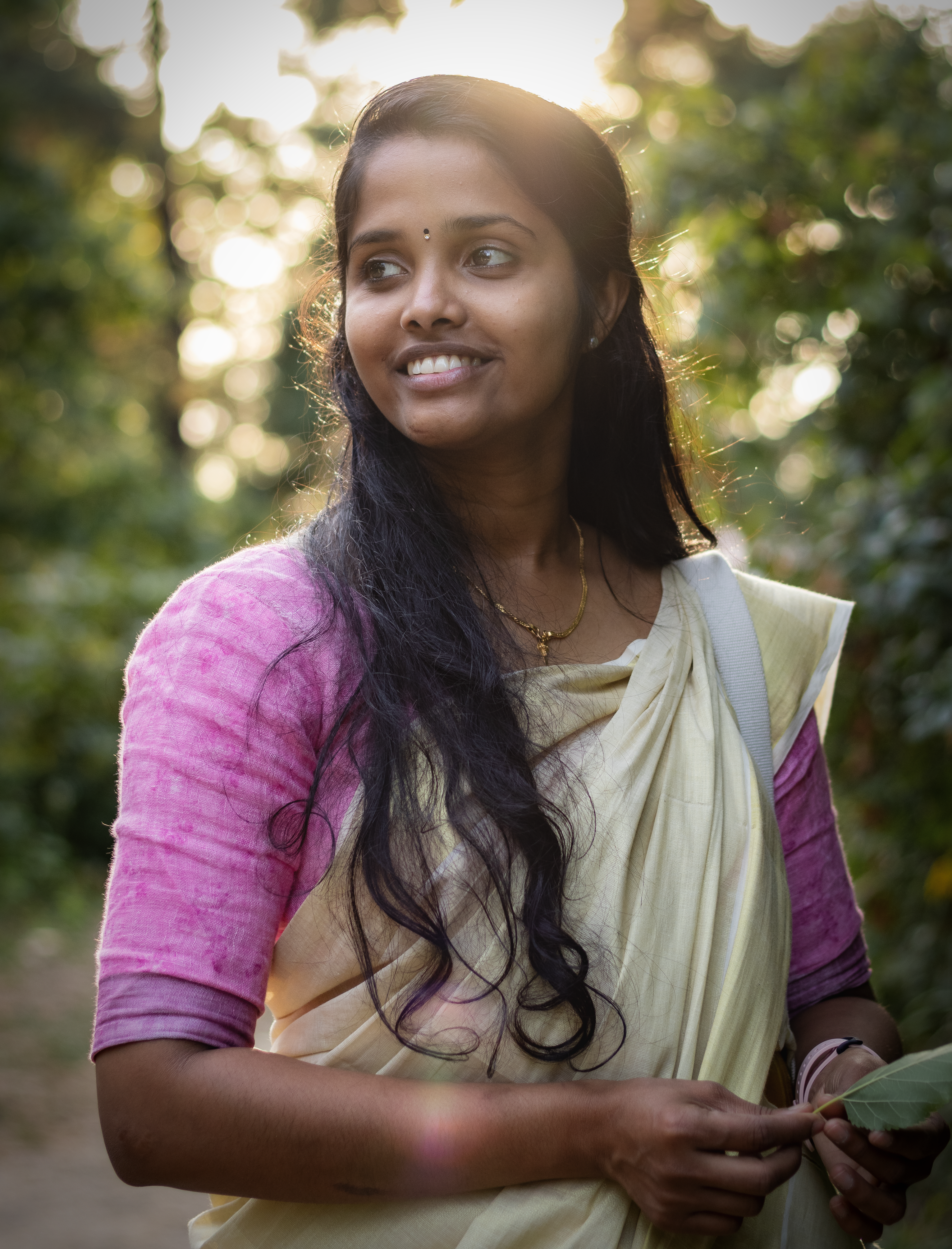 Portrait of a smiling Indian woman in traditional wear with long hair, captured outdoors with natural lighting.