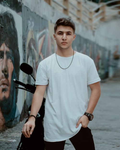 Free Stylish young man stands confidently in an urban alley with vibrant street art. Stock Photo