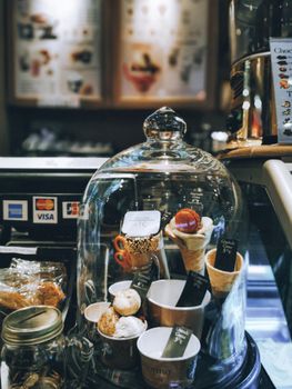 A close-up of delicious pastries and ice cream cones under a glass dome in a cozy coffee shop.