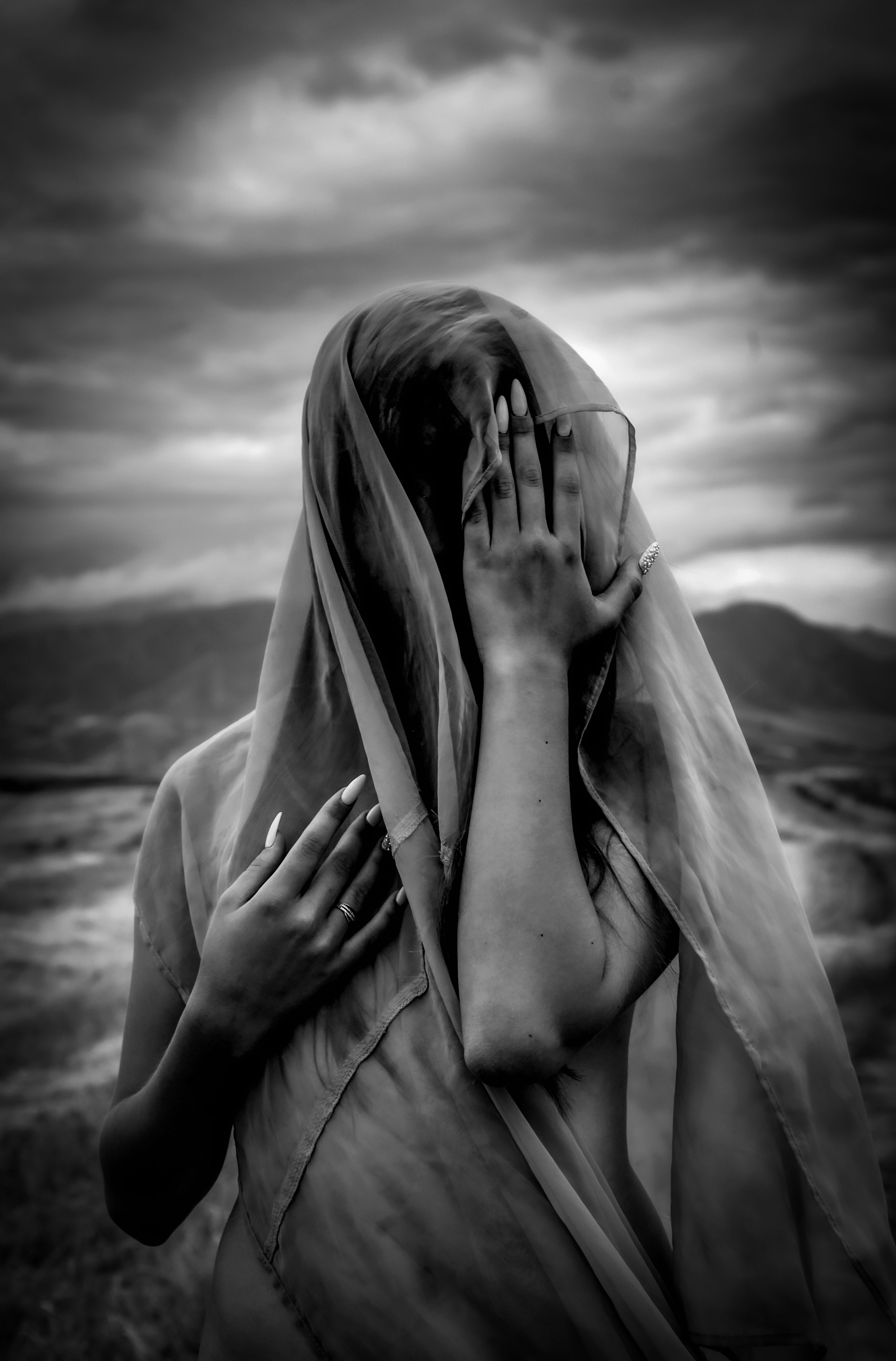 A woman in a fabric veil poses artfully against a dramatic cloudy sky.