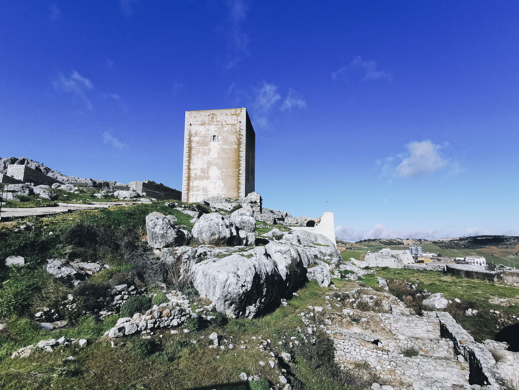 A historic stone tower stands on a rocky hillside under a bright blue sky, showcasing ancient architecture.