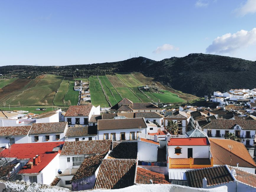 Picturesque Spanish townscape with traditional rooftops and lush hills under a clear sky.