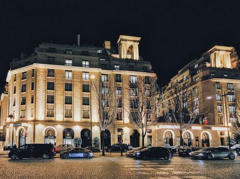 A vibrant night scene featuring illuminated buildings and decorated trees on an urban street.