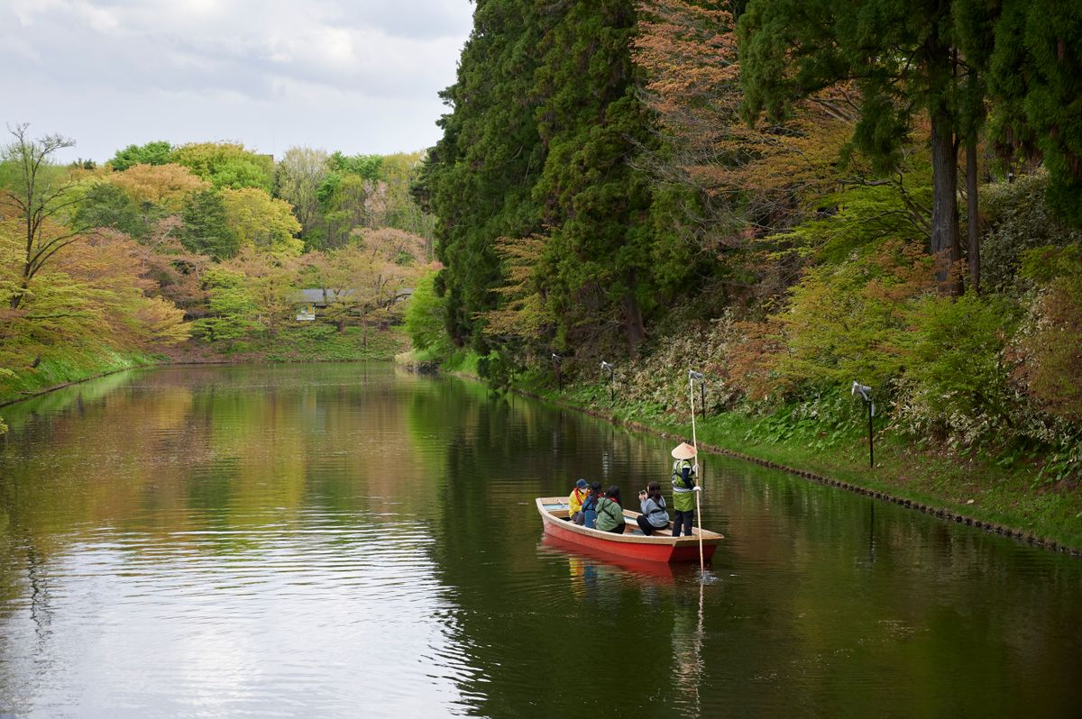 Small red boat on the spring moat at Hirosaki Castle, surrounded by new foliage — the castle park's boat rental operates through the spring and summer season