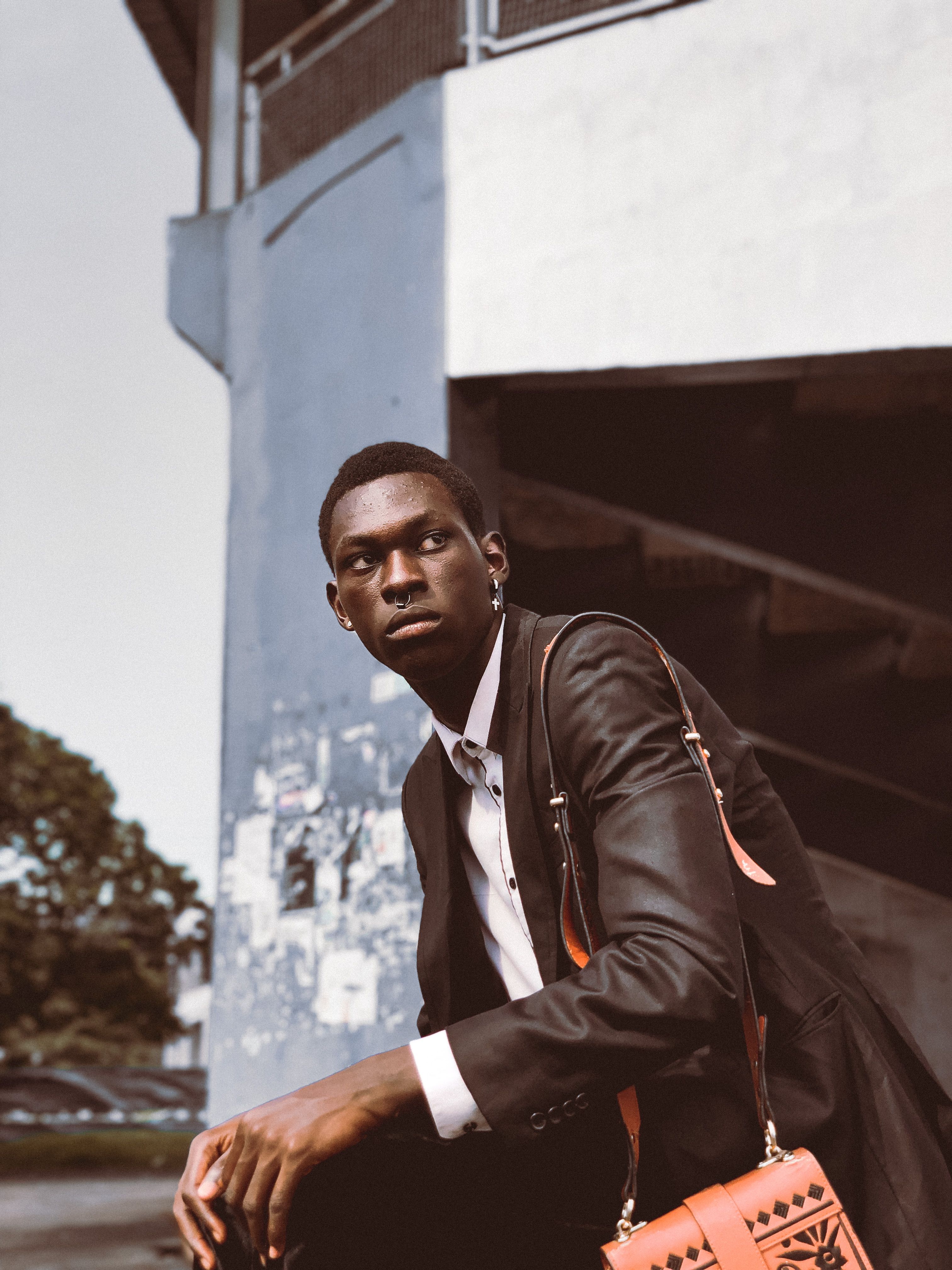 Man in a suit with a fashionable bag sitting outdoors in an urban setting.