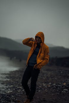 Man in a bright yellow jacket walking on a stormy beach in the evening.