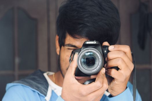 A young man focuses intently while capturing a photo with his DSLR camera indoors.