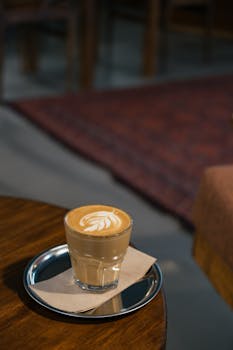 A cozy indoor cafe scene with a cappuccino featuring latte art on a wooden table.