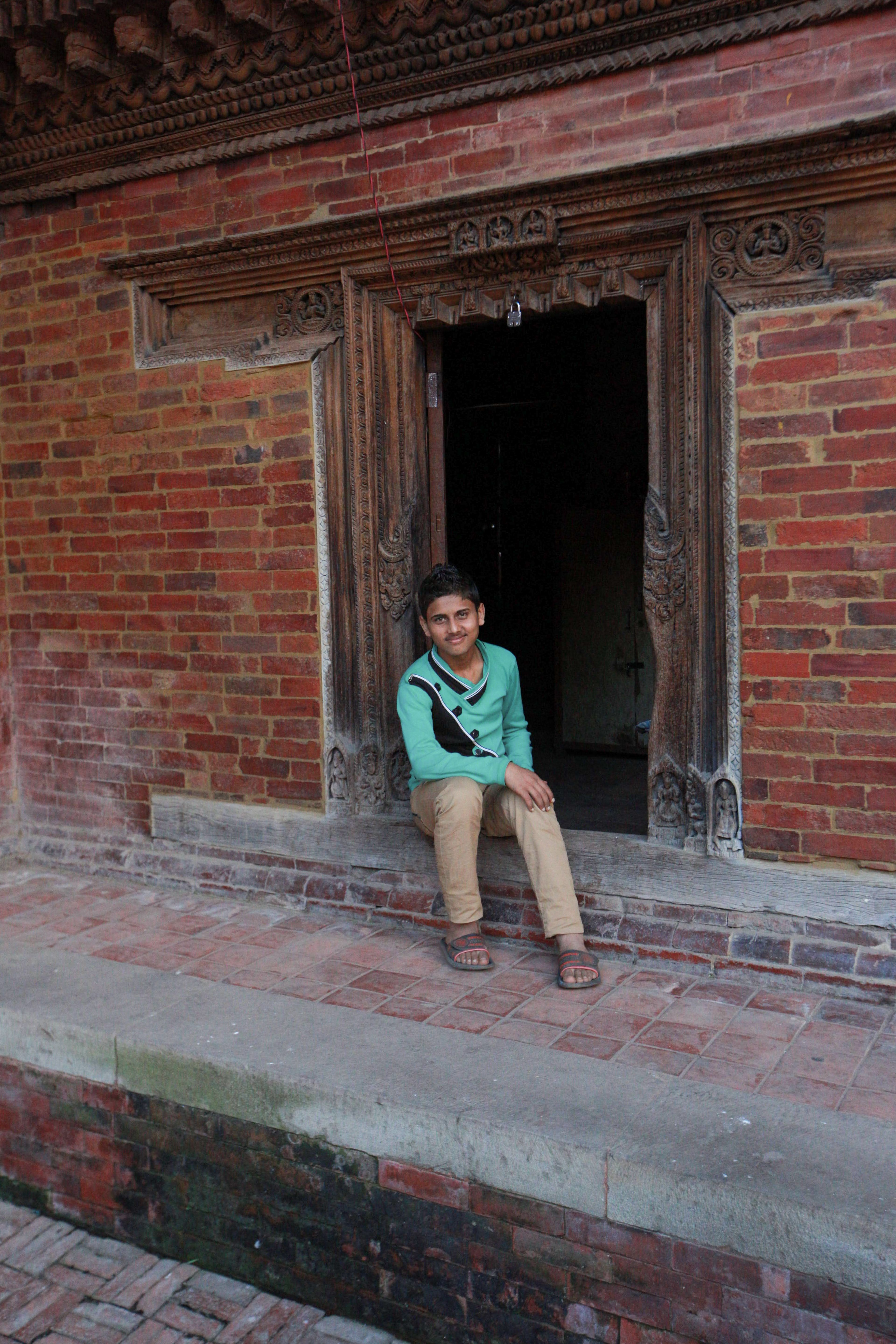 A young man sits casually in an intricately carved brick doorway, exuding cultural charm.