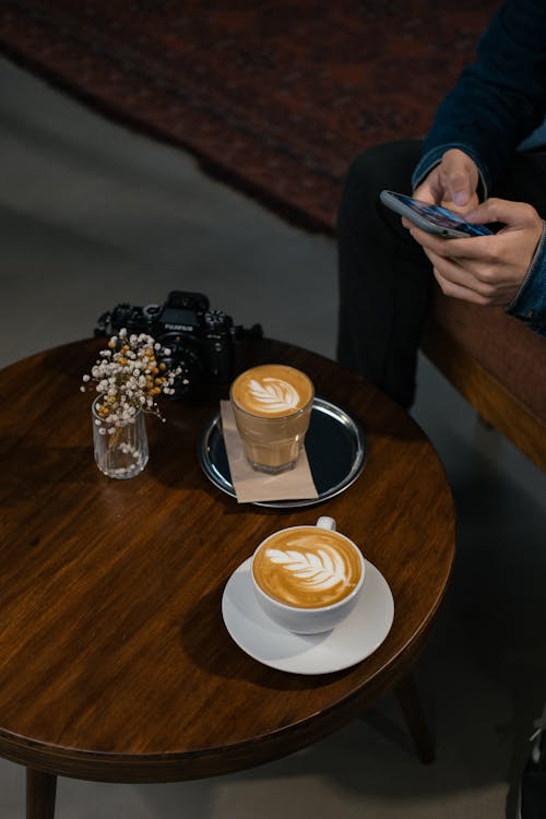 Person Using a Cellphone Beside Cups of Coffee