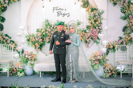 Stunning wedding photo featuring bride in silver gown and groom in military uniform amidst floral decor.