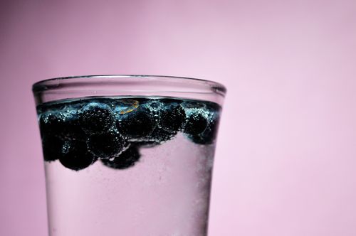 Free A glass of sparkling water with blueberries against a pink background, invoking freshness. Stock Photo
