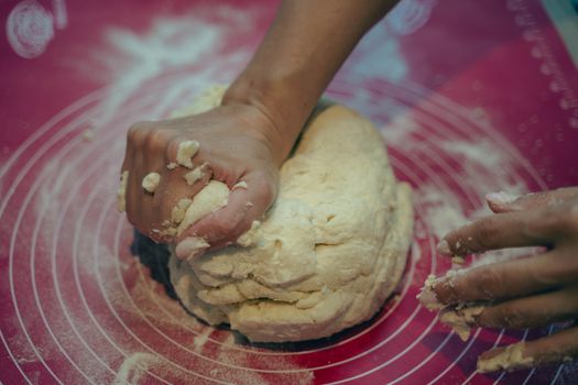 Hands kneading dough on a red surface, showcasing the process of baking and preparation.