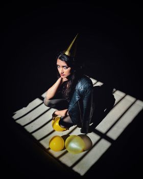 A woman in a leather jacket celebrates in a dramatic light with gold balloons.