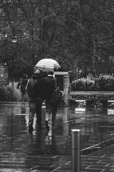 A black and white photo of people walking with umbrellas on a rainy street.