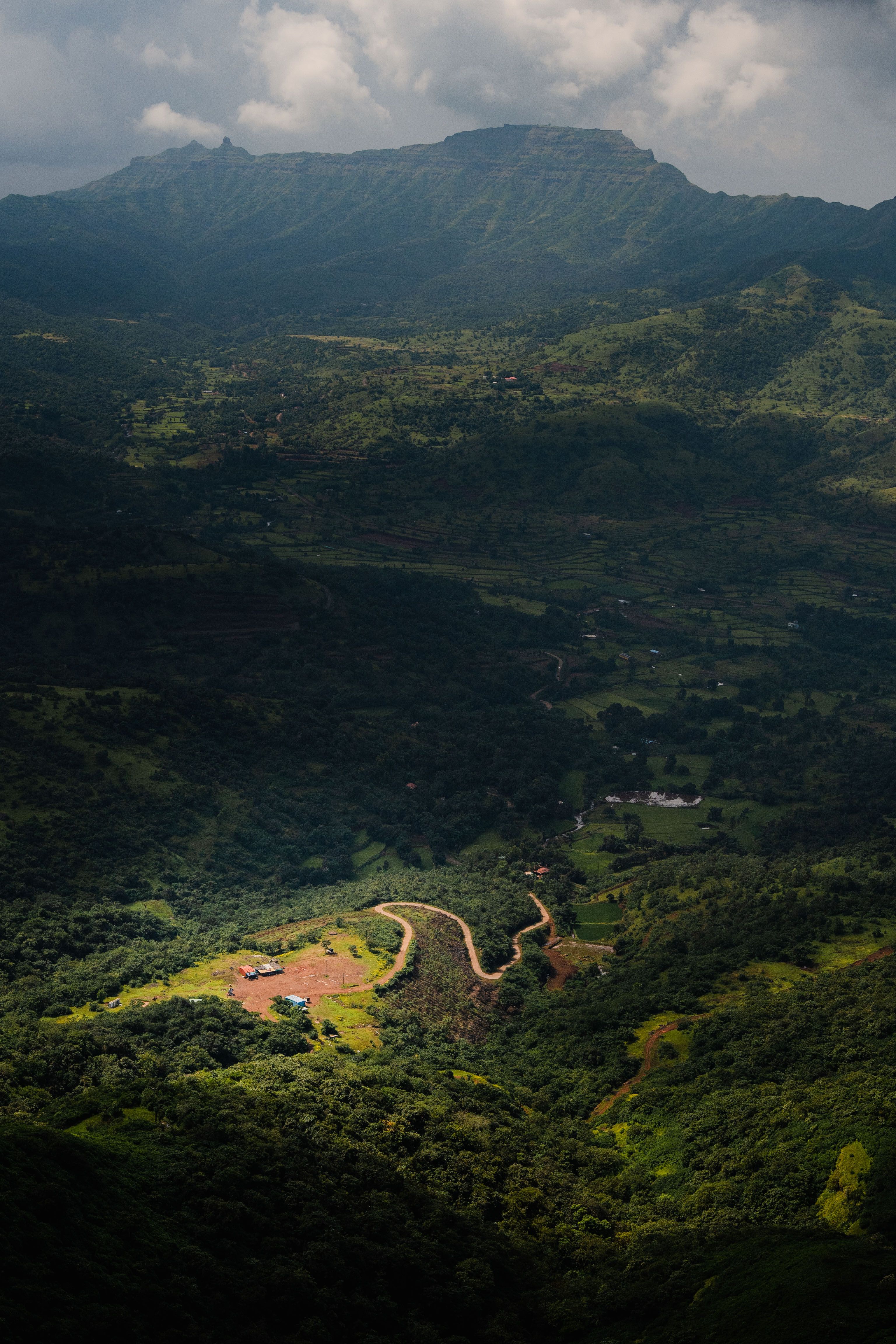 Aerial view of lush green valley and hills under dramatic clouds, showcasing nature's beauty.