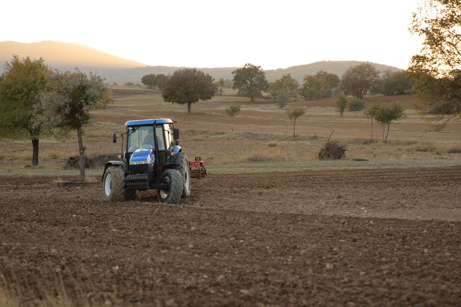 Un tractor cultivando tierras agrícolas al atardecer en un paisaje rural. Perfecto para temas agrícolas.