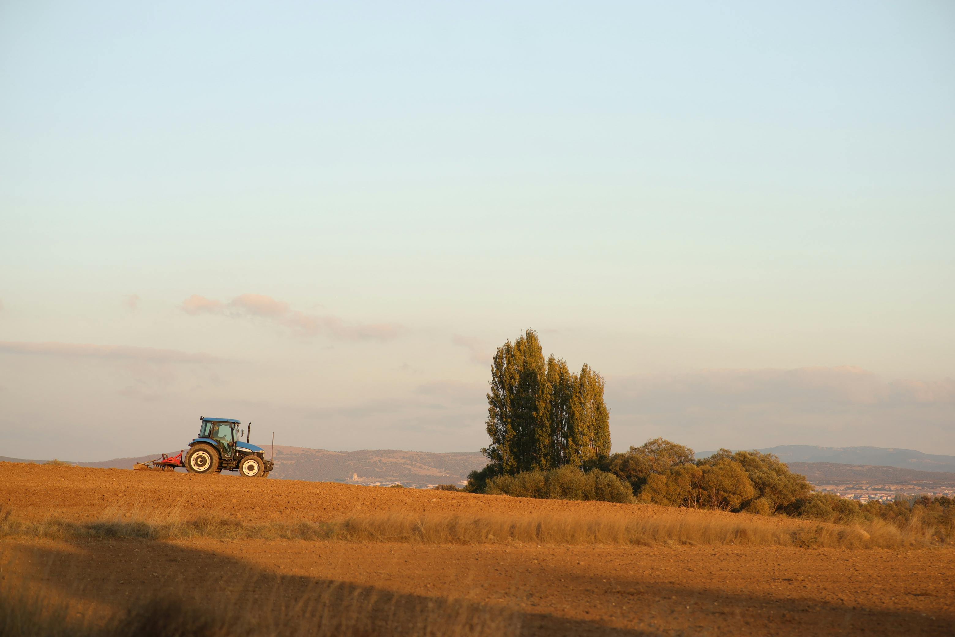 Tractor working on a farm field at sunset, illustrating rural agriculture and machinery in a vast landscape.